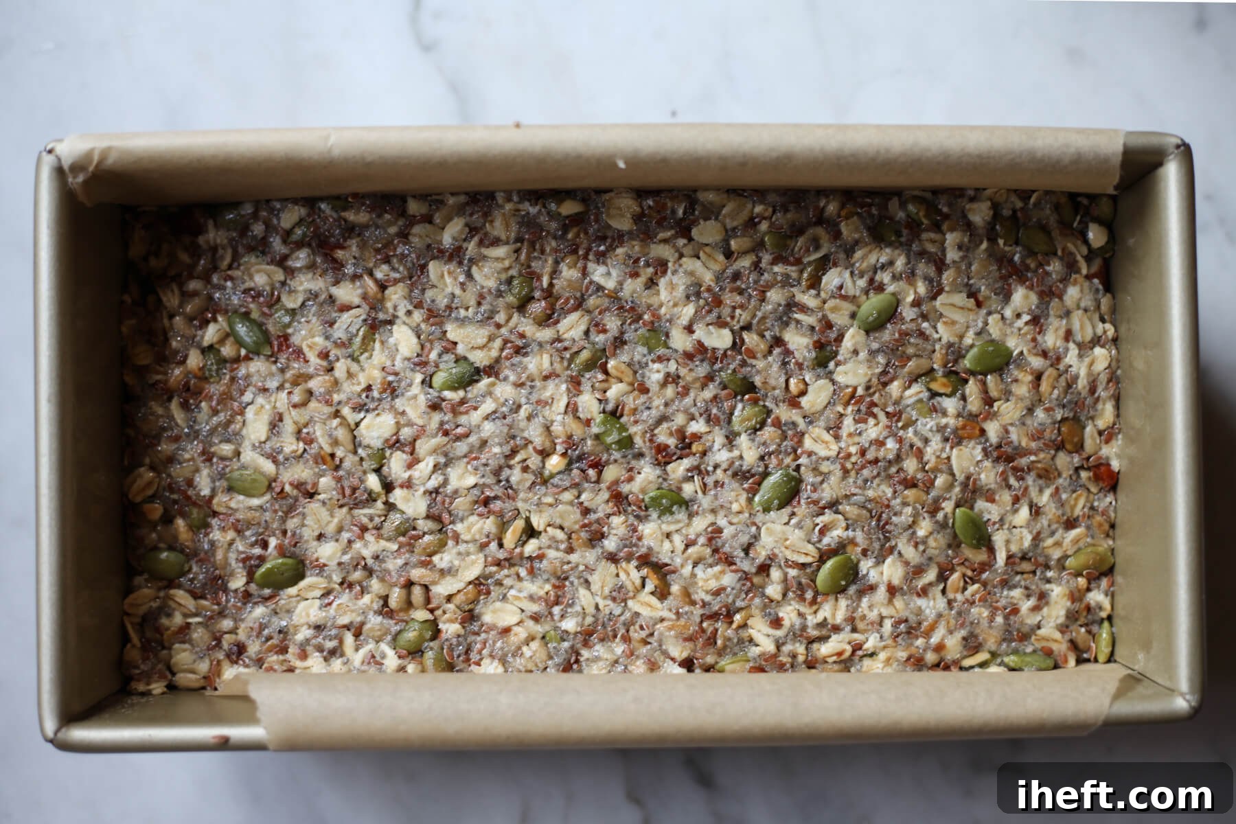 A gold loaf pan filled with adventure seed bread before baking.