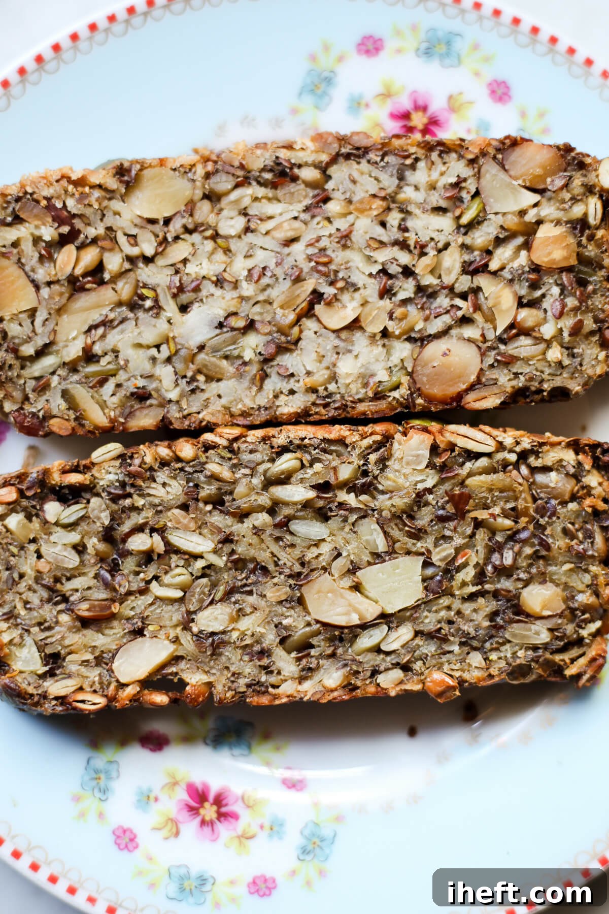 A close-up photo showcasing two perfectly sliced pieces of adventure seed bread, revealing its dense, wholesome texture and rich seed content. 