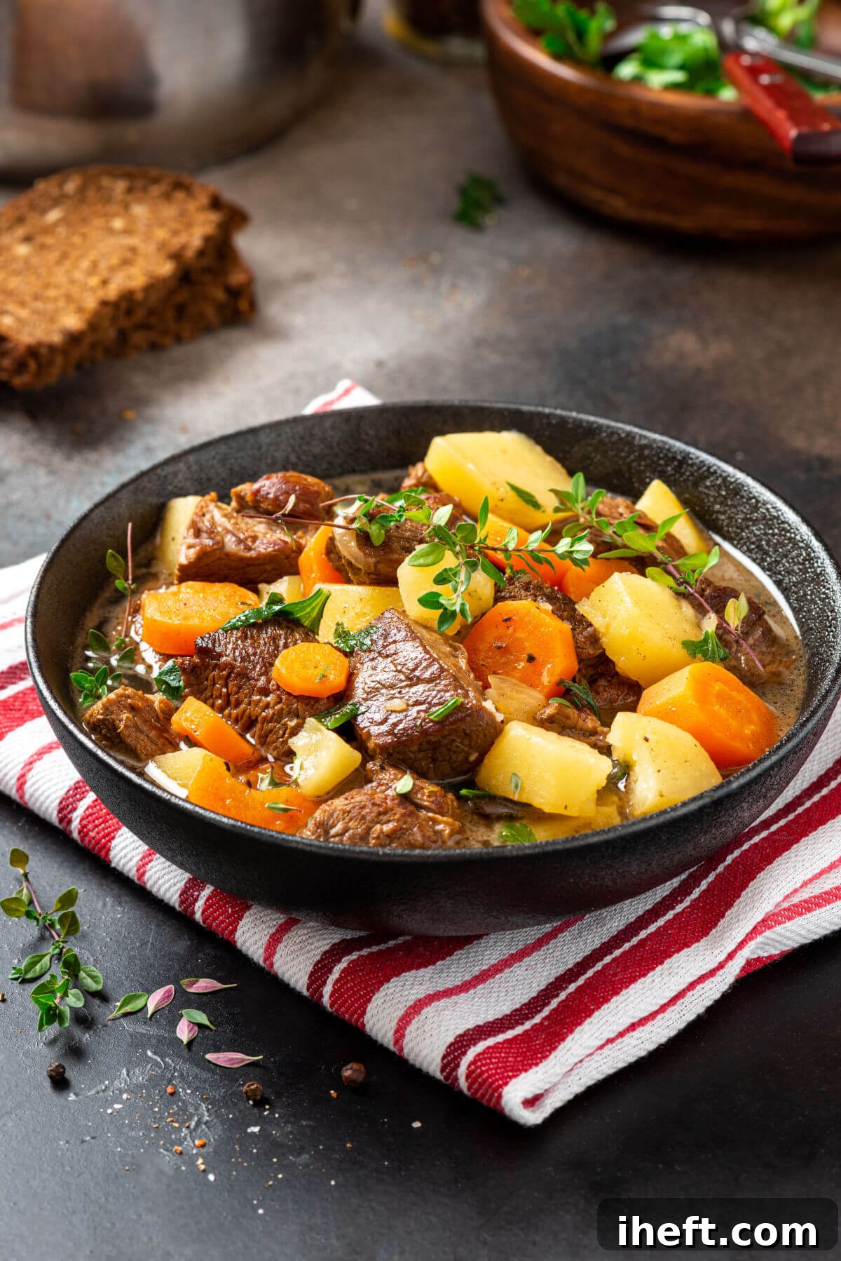 A dark ceramic dish filled with traditional Irish stew made with tender beef, chunky potatoes, and sweet carrots, garnished with fresh thyme. 