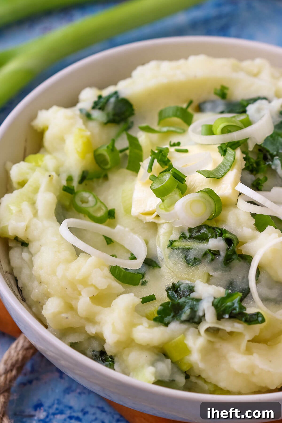 A close-up of vibrant colcannon, a traditional Irish recipe featuring creamy mashed potatoes blended with finely chopped kale, fresh green onions, and tender leeks, showcasing its rustic texture. 