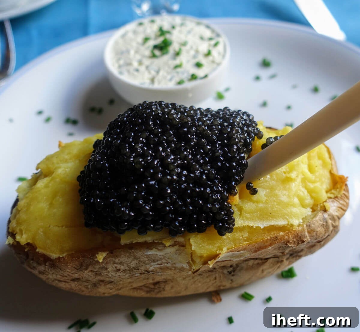 A baked potato with caviar on top from Caviar Kaspia in Paris. The caviar potato is served with a mother of pearl spoon and small dish of creme fraiche with chives. 