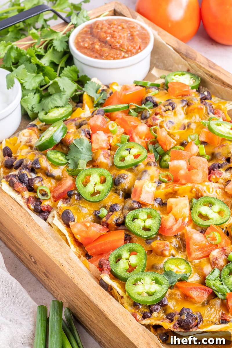 A wooden tray filled with sheet pan vegetarian nachos topped with melted cheese, jalapeno, tomato, cilantro, salsa, and sour cream. This tray of nachos looks perfect for a party. 