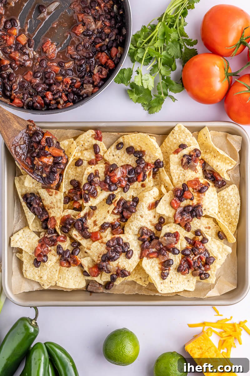 Tortilla chips on a sheet pan topped with seasoned black beans.