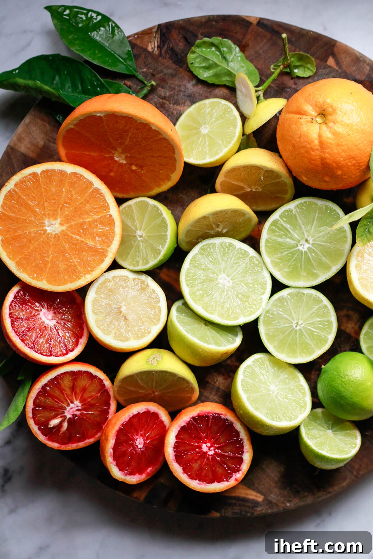 Vibrant colors of citrus cut in half: limes, blood oranges, and orange oranges on a cutting board. 