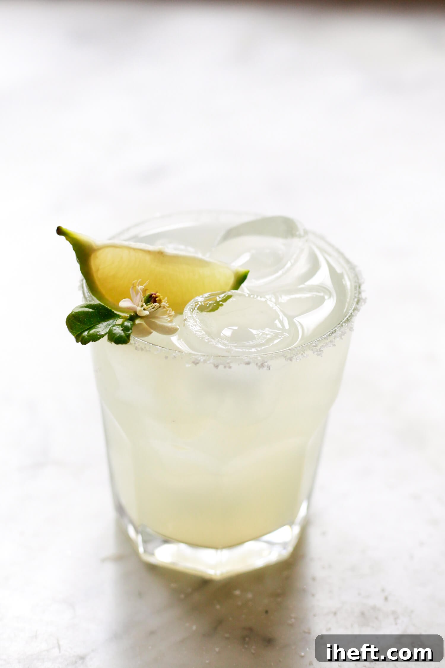 A beautiful Cadillac Margarita with a salt rim on the rocks garnished with lime and a lime flower on a marble countertop. 