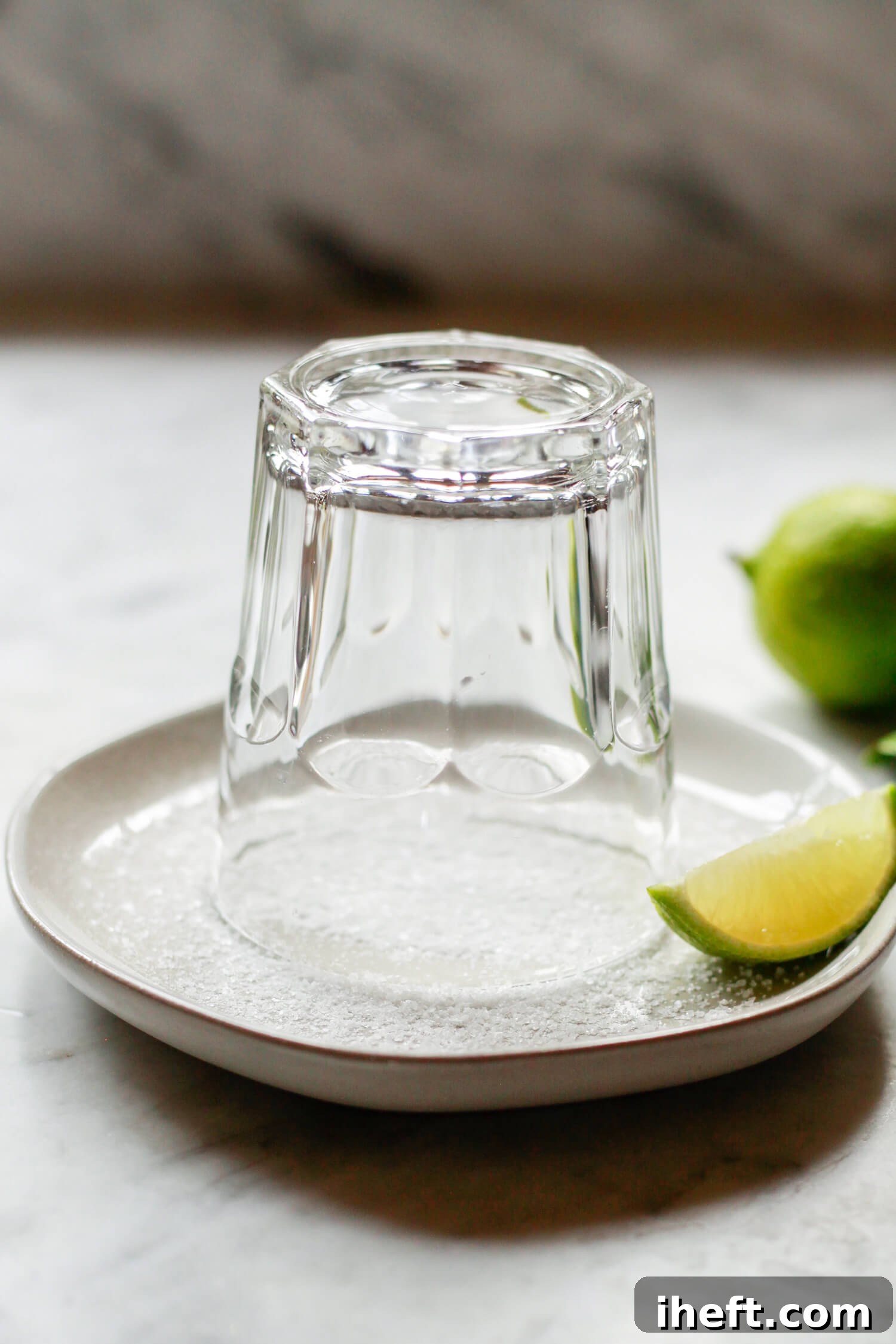 A rocks glass inverted on a small dish of salt with a lime on the side. This is how you make a salt rim for a Cadillac Margarita. 