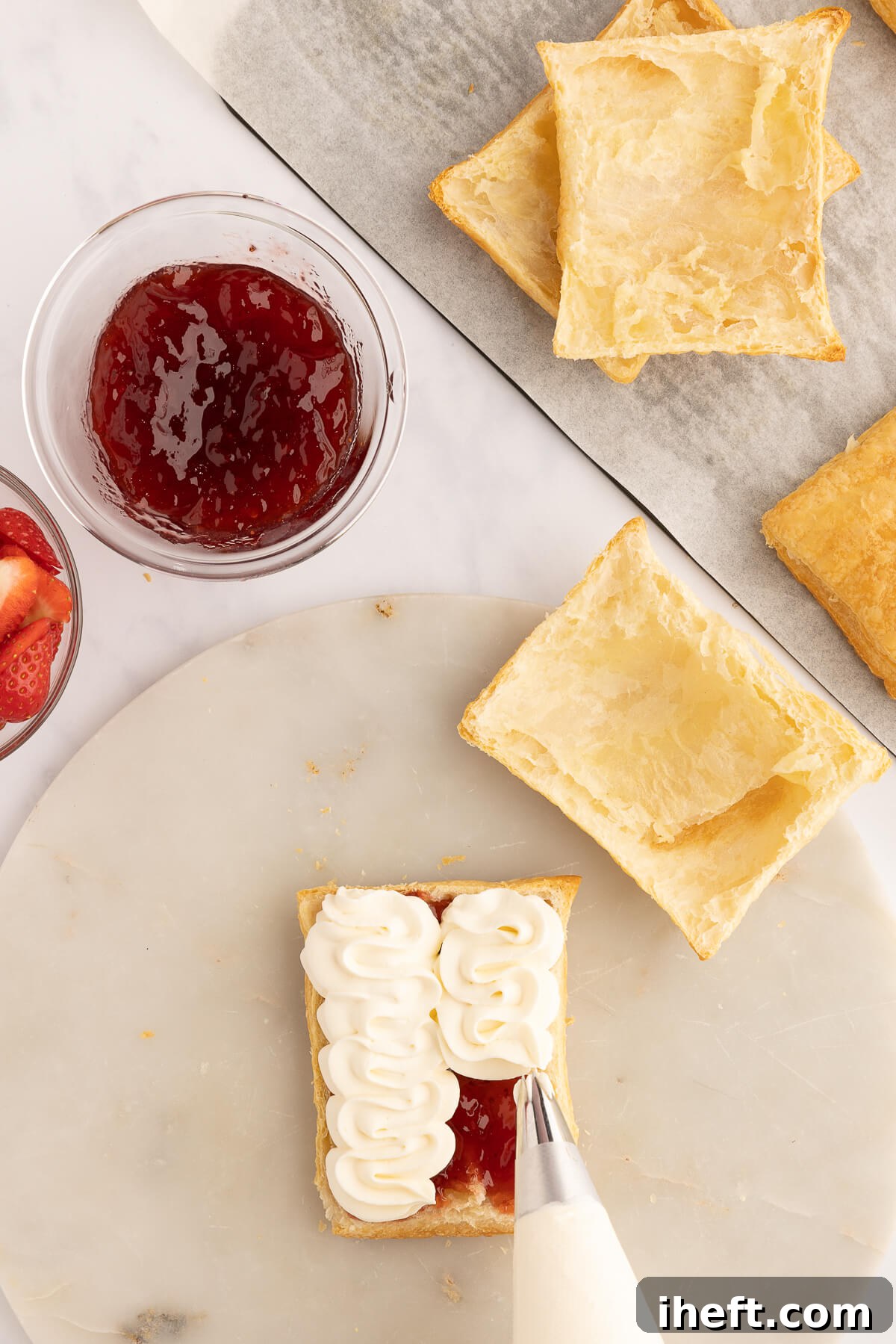 Layering a Napoleon dessert with cream in a piping bag and strawberry jam.