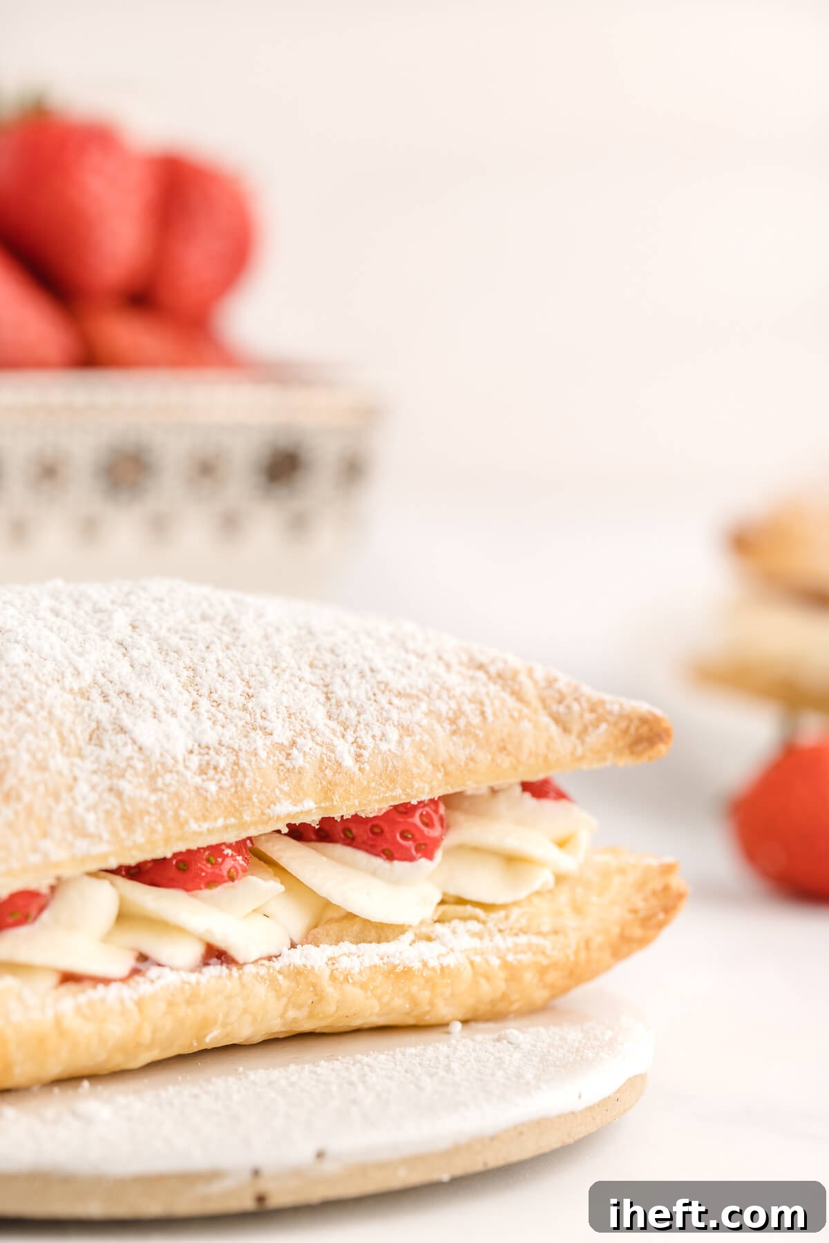 A close up photo of a Strawberry Napoleon with beautiful swirls of cream topped with sliced strawberries inside layers of puff pastry. 