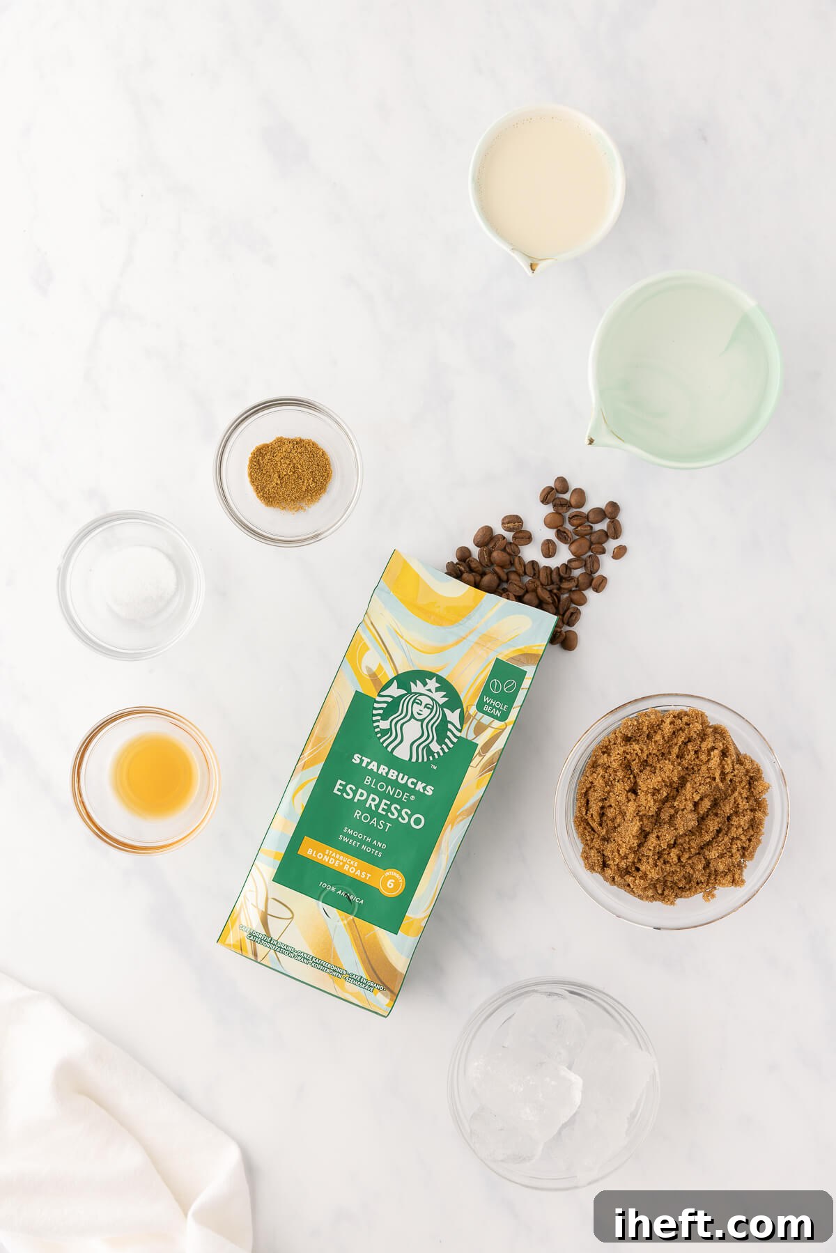 The ingredients for a homemade brown sugar shaken espresso on a marble countertop. This includes Starbucks blonde espresso coffee beans, brown sugar, ice, oatmilk, cinnamon, vanilla, and salt. 