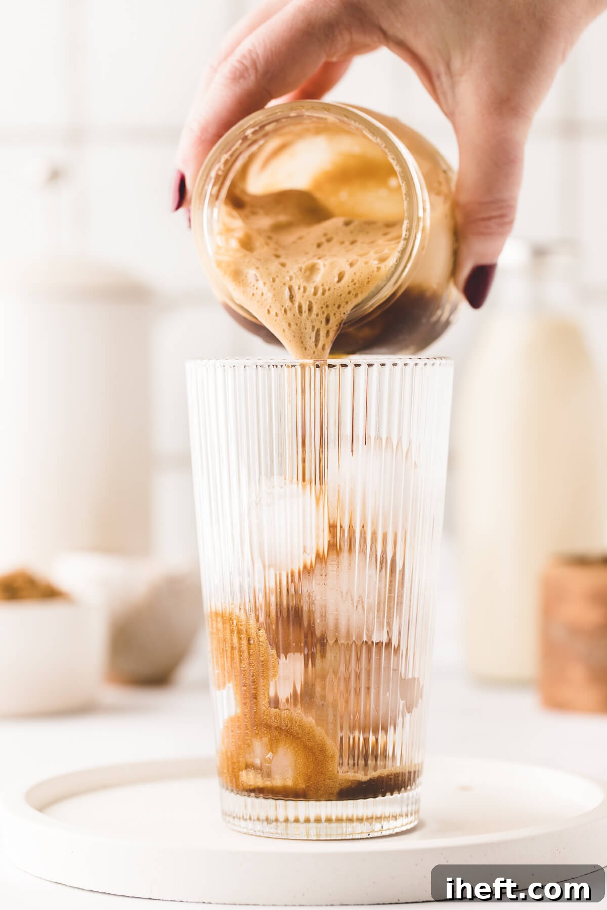 Shaken espresso in a mason jar is poured into a tall glass of ice.