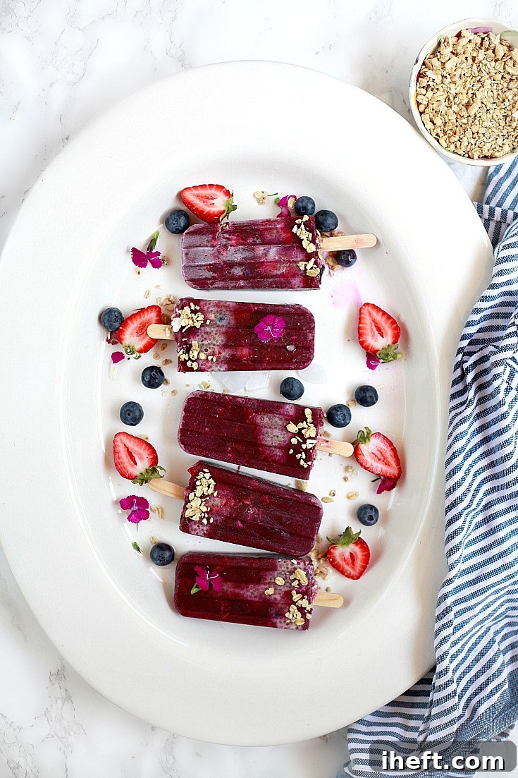 A beautiful platter of acai and chia popsicles with granola and berries, garnished with edible flowers. 