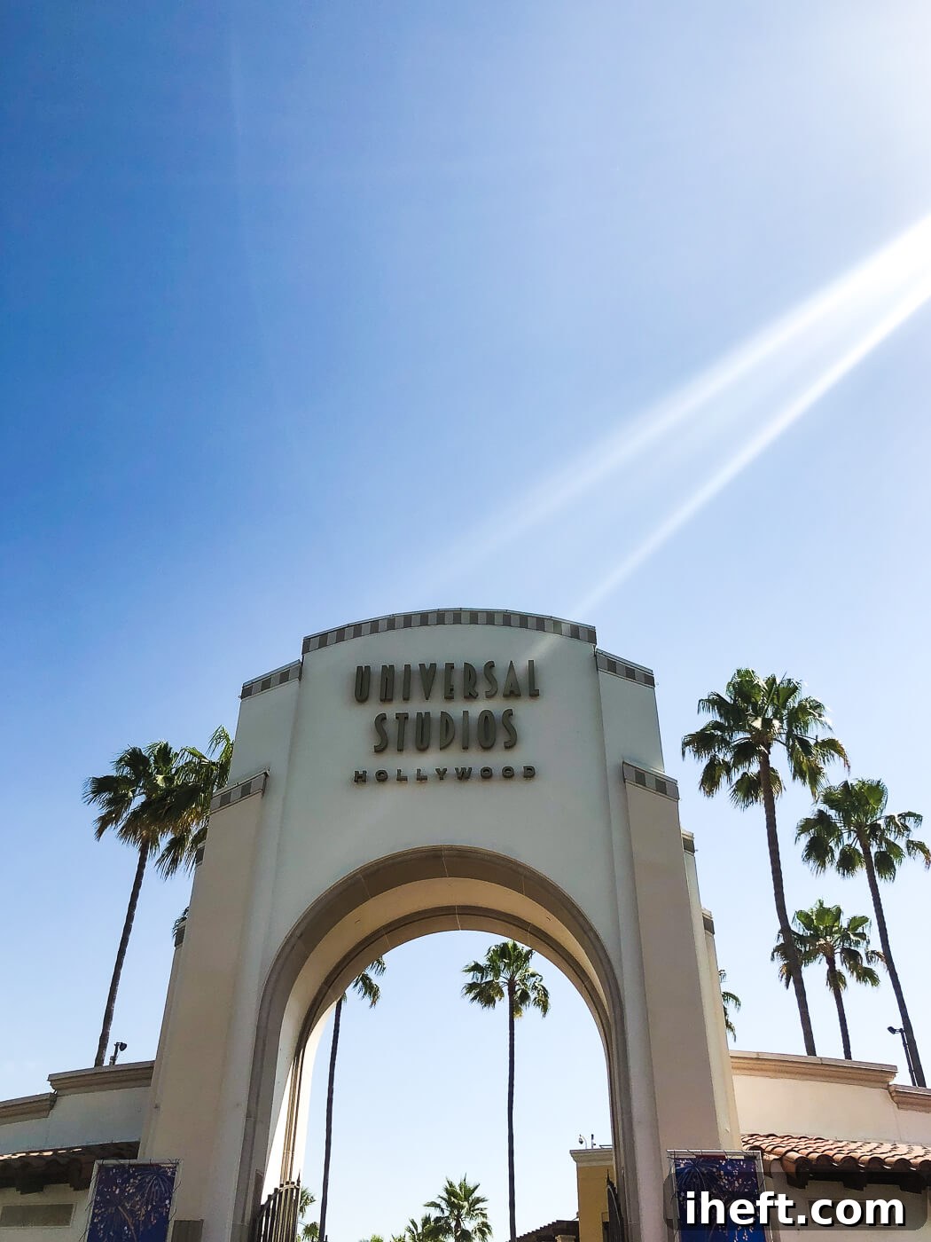 The grand, iconic arched entrance to Universal Studios Hollywood, framed by swaying palm trees against a clear blue sky, inviting visitors into a world of cinematic adventure.
