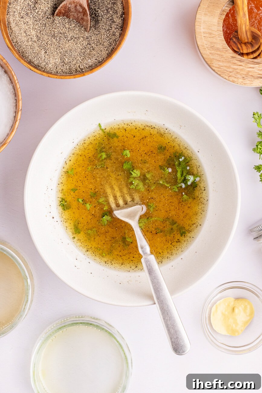The ingredients for a homemade vinaigrette for sweet potato salad are combined in a white bowl with a fork.