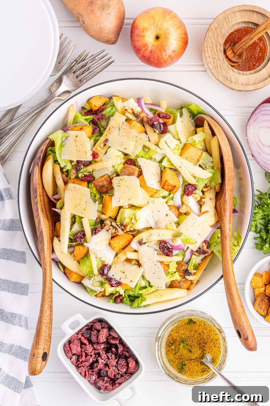 A beautiful large white salad bowl filled with a Thanksgiving salad made with romaine lettuce, roasted sweet potatoes, cranberries, apples, onions, parmesan, and nuts. This is an overhead photo of a delicious fall salad. 