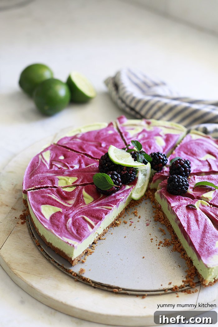 A vegan cashew lime pie with beautiful pink blackberry swirls on top, resting on a clean white kitchen counter. The pie has a light green base, contrasting elegantly with the pink and suggesting a fresh, natural dessert.