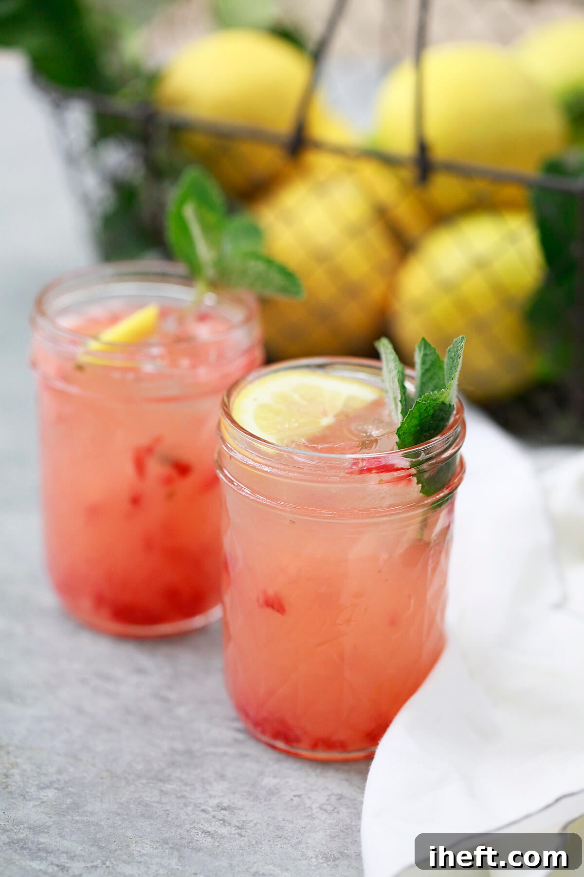 Two clear glasses filled with vibrant homemade strawberry pink lemonade, complete with ice cubes and sliced strawberries, capturing a refreshing and inviting summer drink.