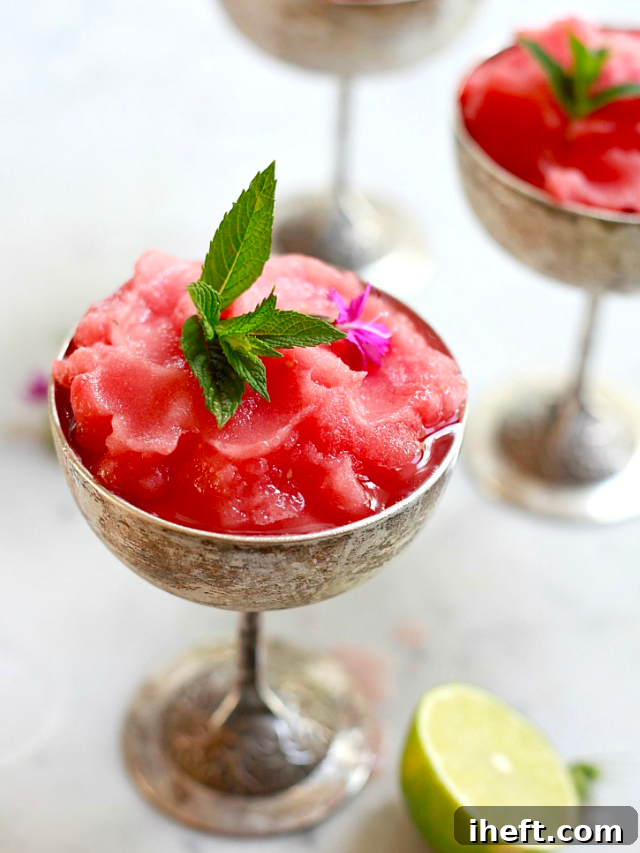 A close-up of a glass filled with Watermelon Frosé (Frozen Rosé), garnished with a slice of watermelon, highlighting the frosty texture and refreshing pink color, perfect for a summer gathering.