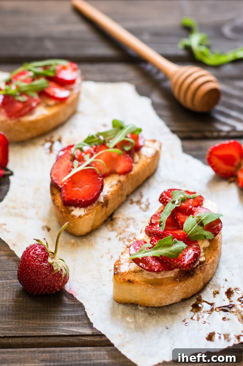 Three pieces of perfectly toasted Italian bread, artfully topped with creamy goat cheese, vibrant fresh strawberries, a drizzle of balsamic glaze, and a scattering of fresh arugula. This image beautifully captures a perfect pink snack idea, showcasing its elegant and delicious components.