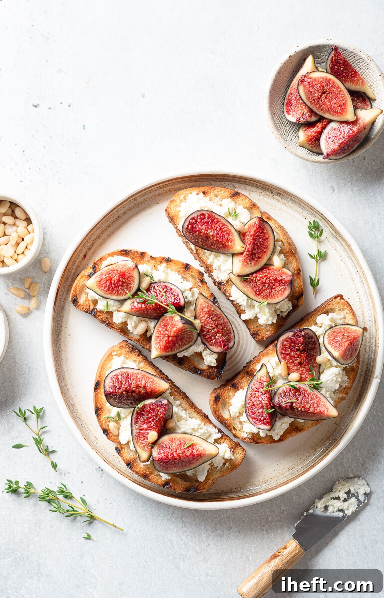 Close-up of fresh figs artfully arranged atop slices of grilled bread, complemented by creamy white cheese, sprigs of fresh thyme, and a sprinkle of pine nuts. This visually appealing dish is highlighted as a great option for pink party food, showcasing its gourmet and natural elements.