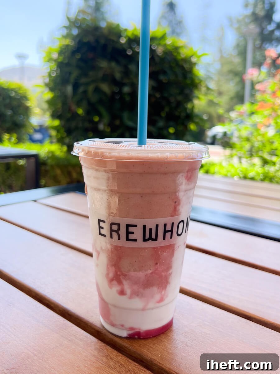 A pink Hailey Beiber Erewhon smoothie in a plastic cup that says EREWHON sits on a wood table outside at Erewhon in Calabasas, CA. 