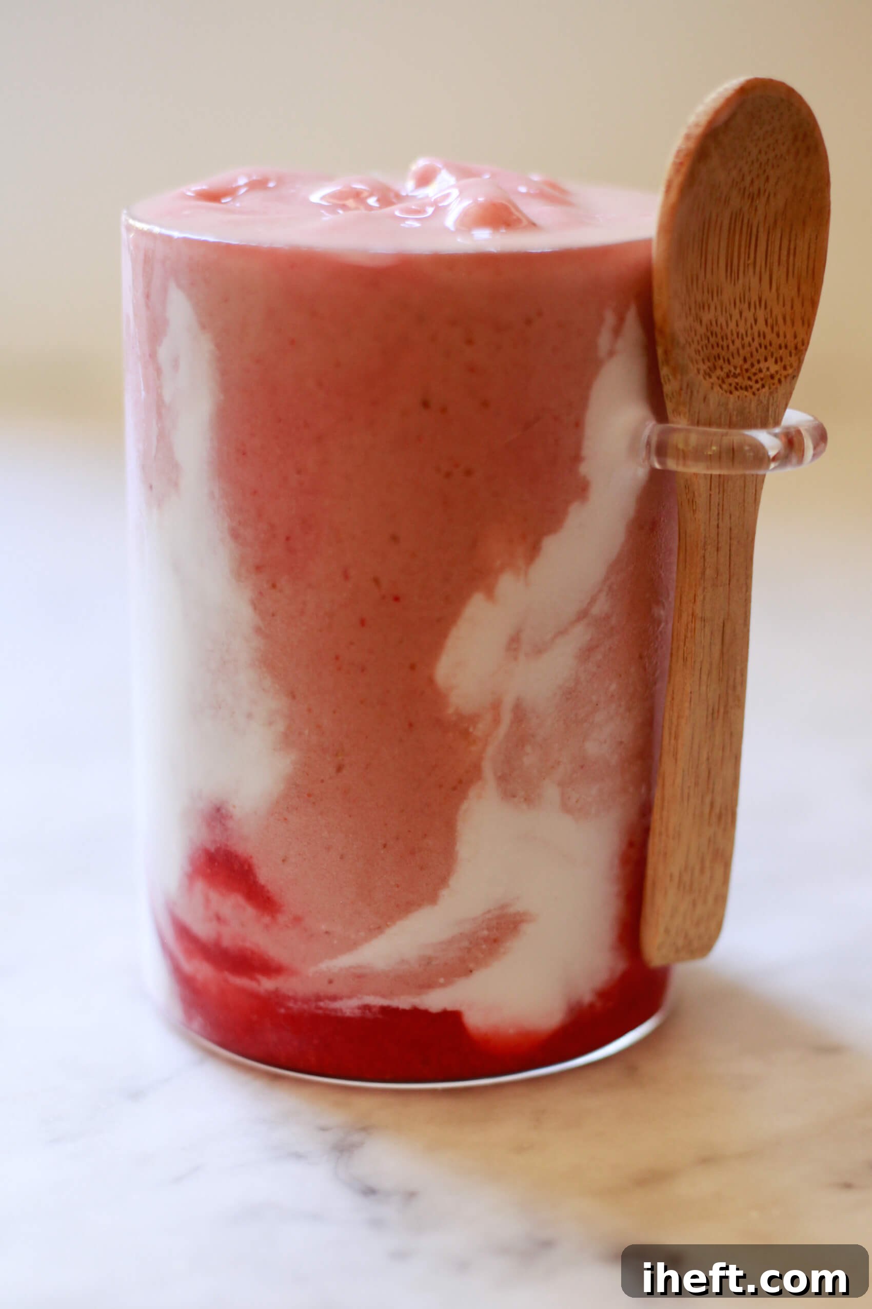 Close-up photo of a homemade Hailey Bieber skin smoothie with coconut cream and strawberry glaze swirls.