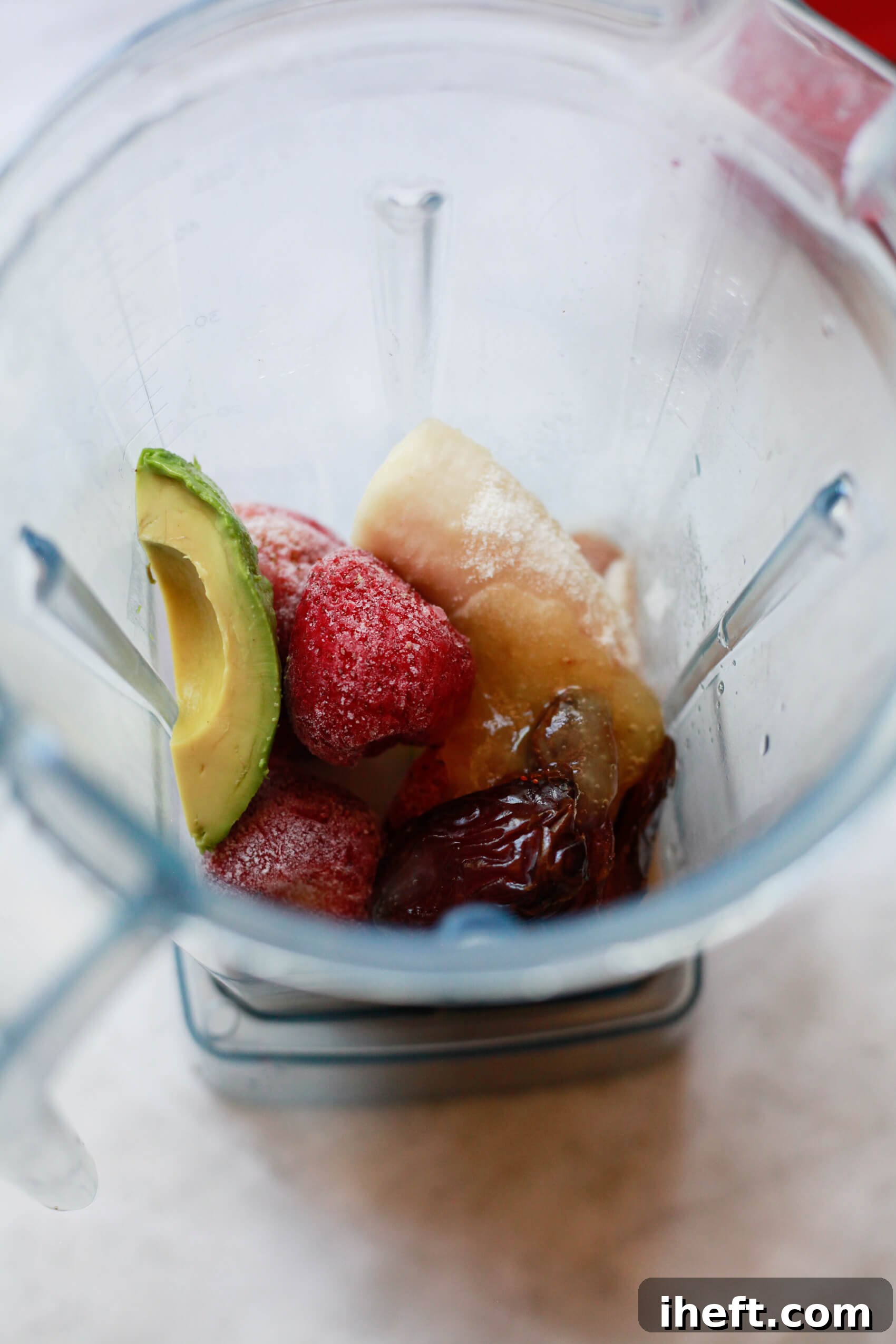 Frozen strawberries, avocado, banana, dates, almond milk, and sea moss gel can be seen in a Vitamix blender before blending into a smoothie. 
