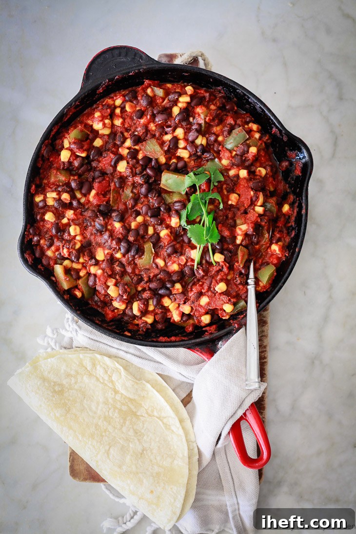 A large skillet brimming with a rich, dark black bean and corn enchilada filling, featuring visible pieces of bell pepper and corn, ready to be rolled into delicious vegetarian enchiladas.