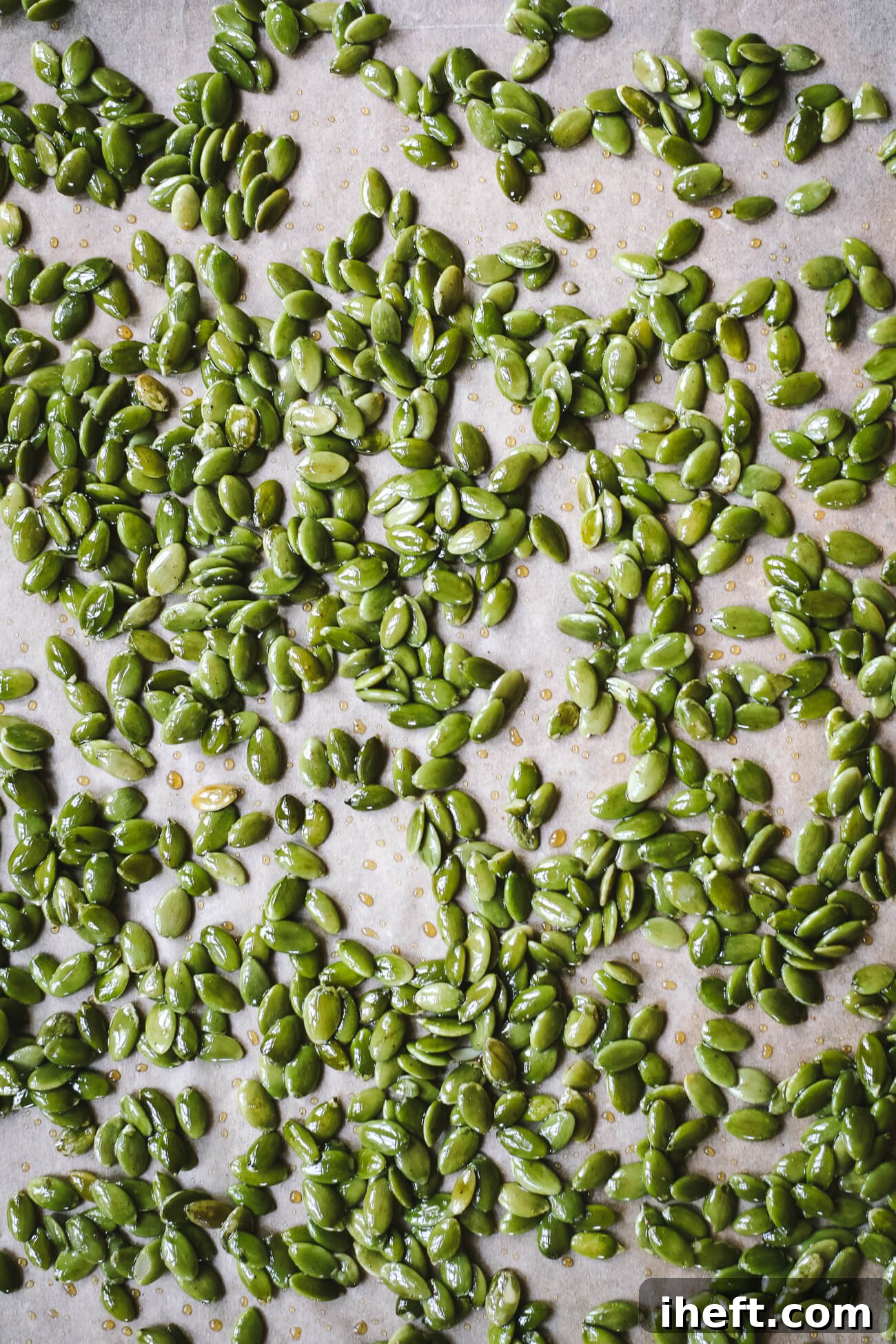 Green raw pepitas coated with a maple glaze on a parchment-lined baking sheet before going into the oven.