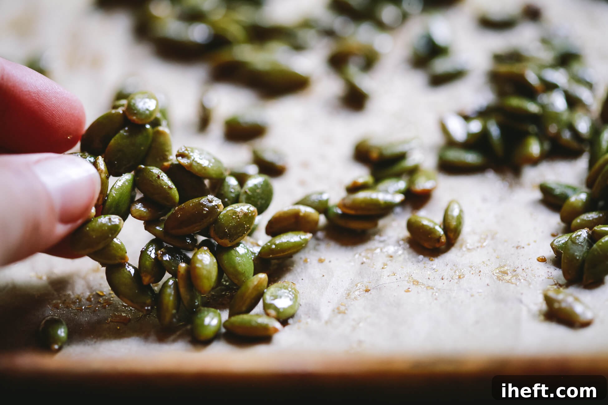 Fingers hold maple roasted pepitas over a baking sheet.