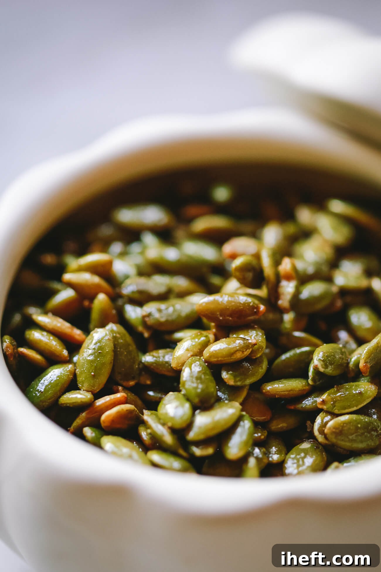 A close-up photo of maple glazed roasted pepitas in a white bowl.