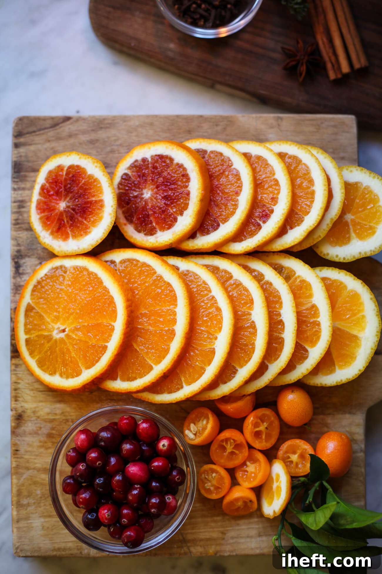 Sliced oranges and kumquats on a cutting board with a bowl of cranberries. 