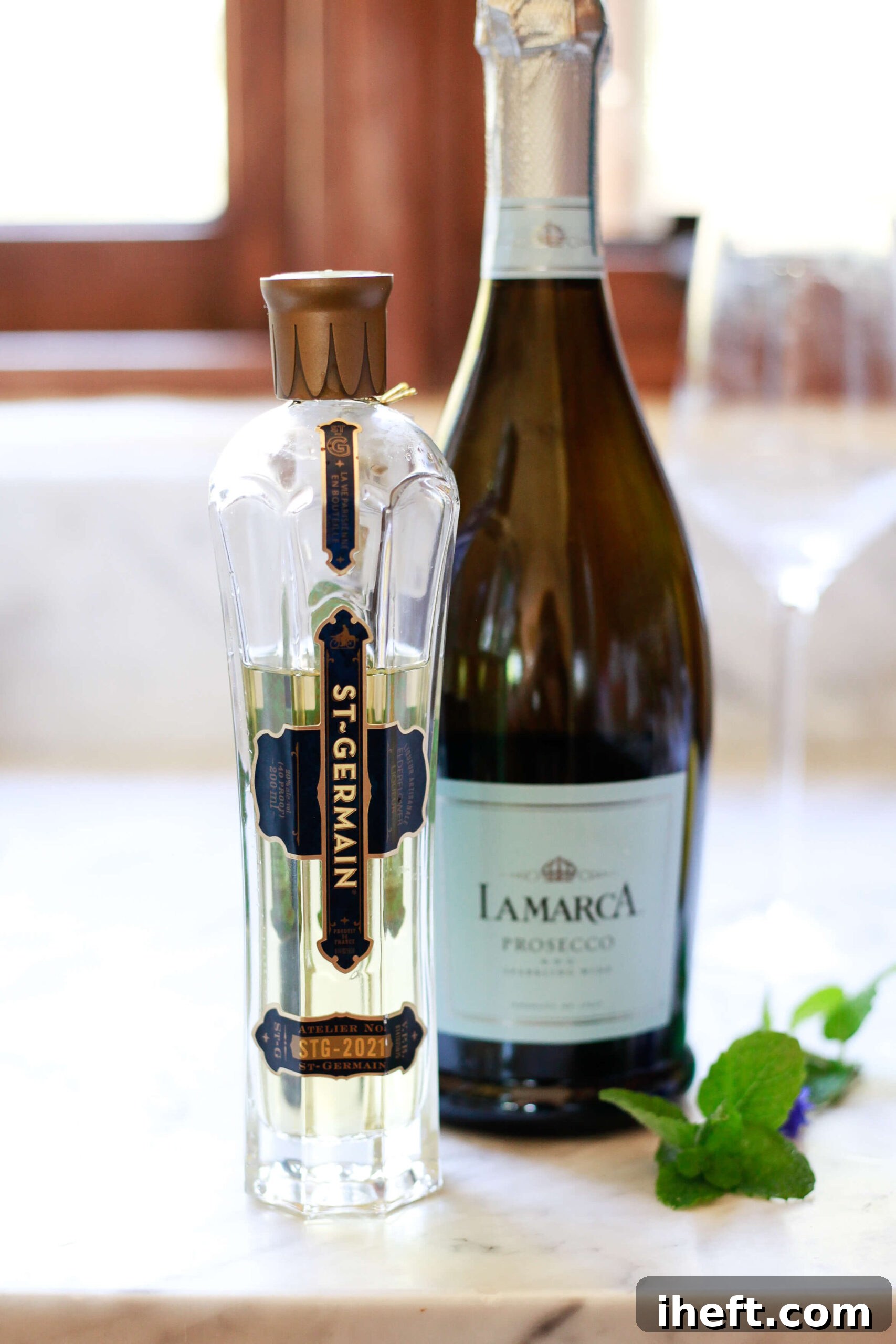 A bottle of St. Germain and LaMarca Prosecco sit on a marble countertop with fresh mint and a wine glass in the background. 