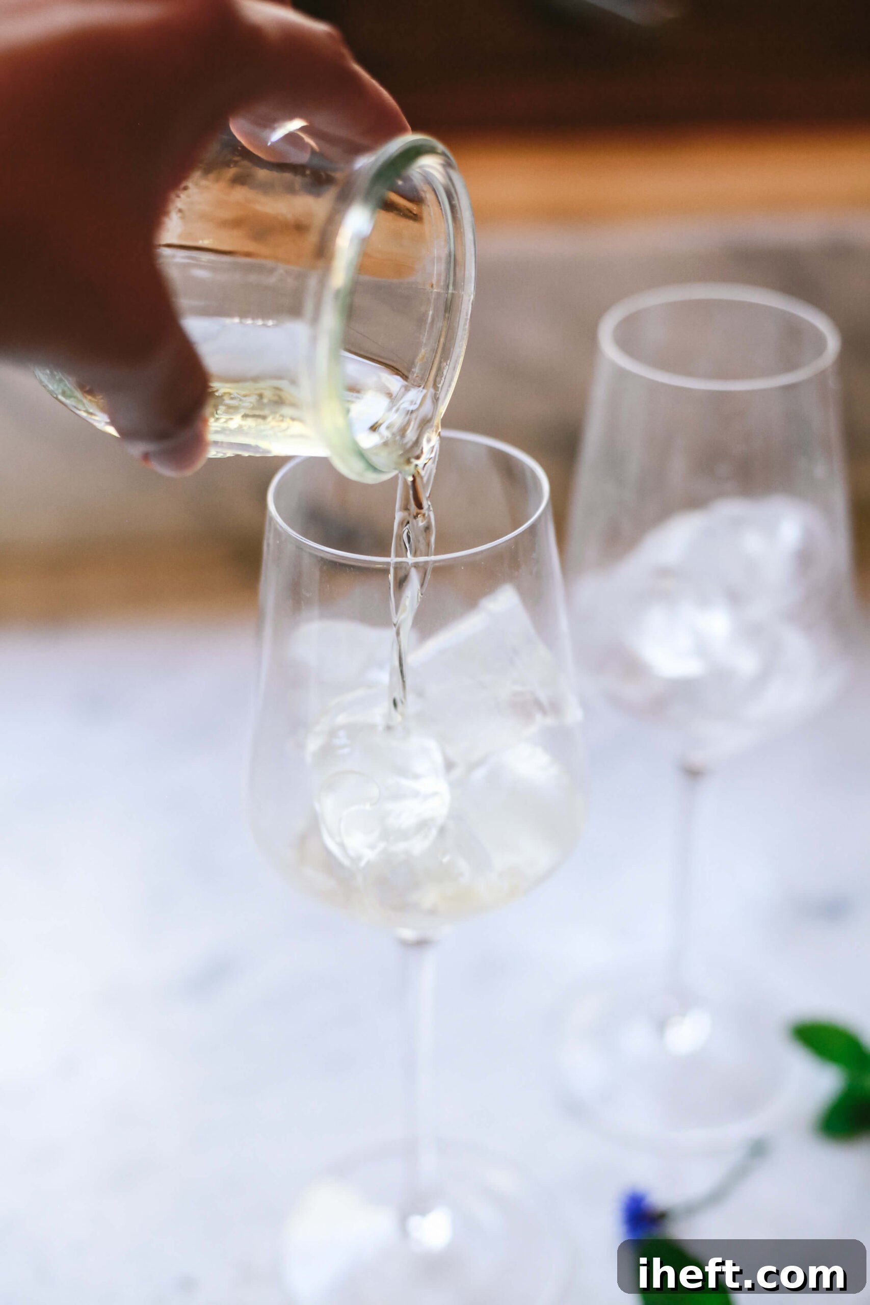 St. Germain elderflower liqueur is poured into a wine glass with ice.
