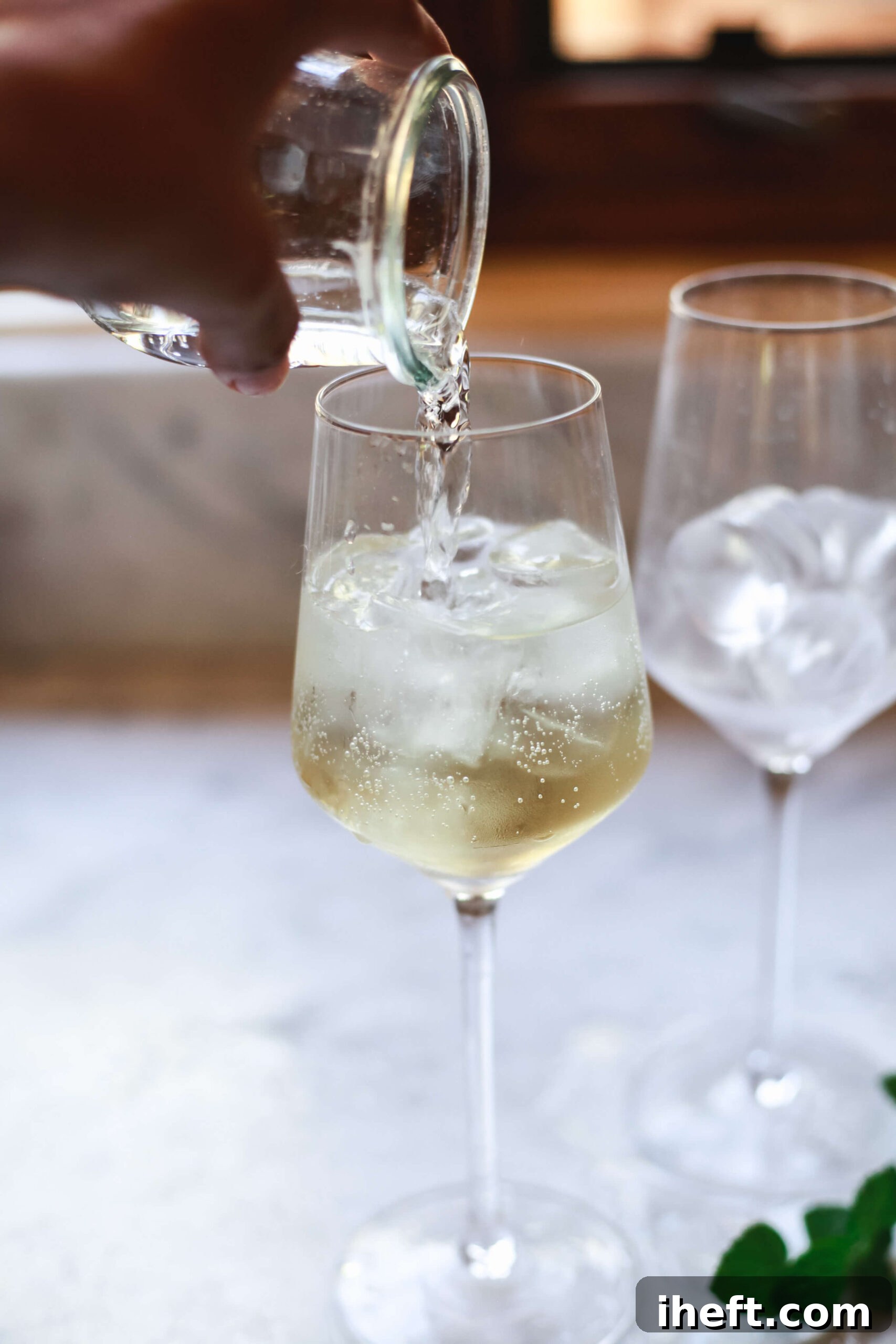 Prosecco is poured over St. Germain and ice in a wine glass to make a Hugo Spritz.