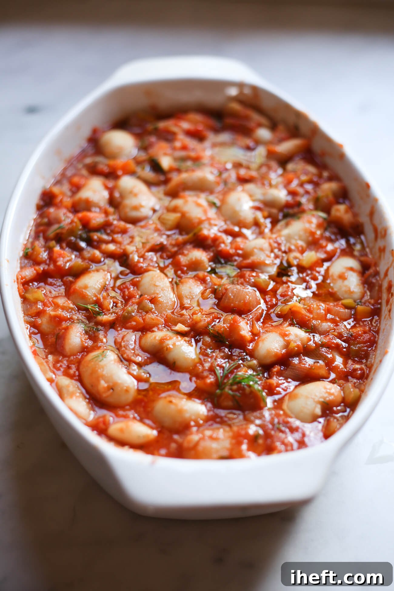 A pristine white casserole dish showcases plump Gigantes beans bathed in rich tomato sauce, perfectly prepped and ready for baking into the delicious Gigantes Plaki.