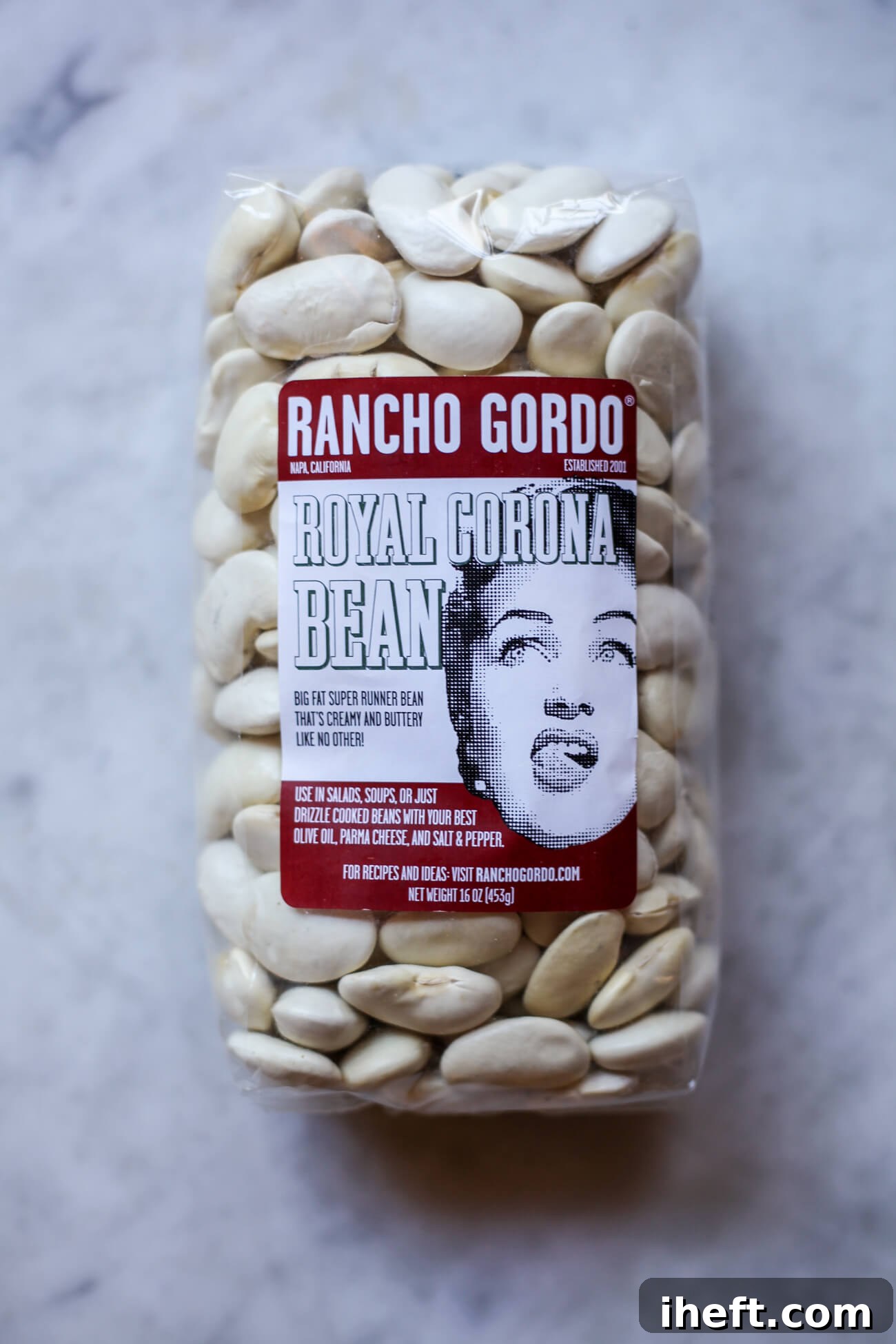 A 1-pound package of premium Rancho Gordo Royal Corona beans, an excellent substitute for traditional Gigantes, resting on a clean marble countertop, ready for use in a delicious Greek recipe.