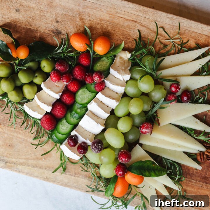 A cheese charcuterie board in the shape of a Christmas tree, garnished with fresh rosemary and a star cracker.