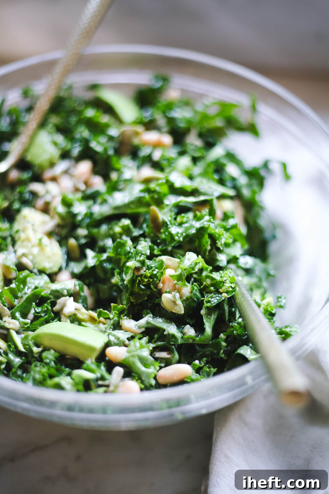 A close up photo of a tossed kale and white bean salad with avocado and seeds. 