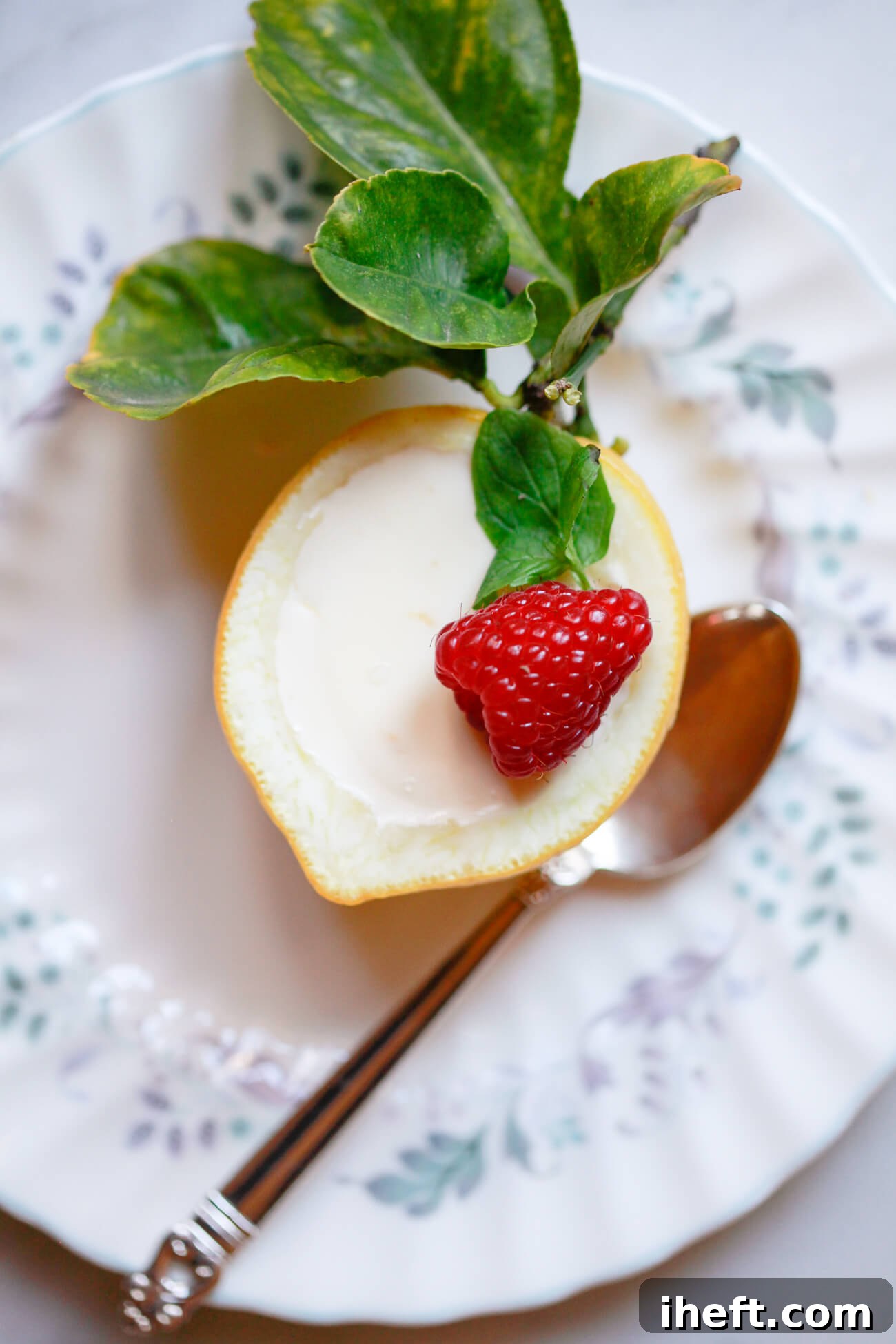 A lemon posset (lemon cream) served in half of a lemon shell with a raspberry and mint sprig. 