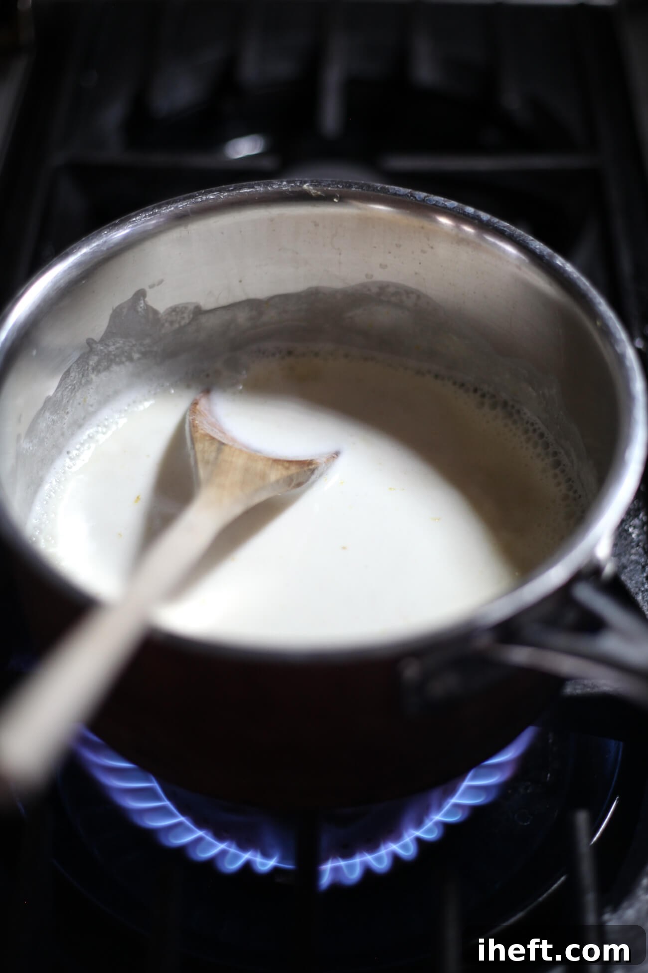 Cream, sugar, and lemon zest in a saucepan with a wooden spoon on a stove.