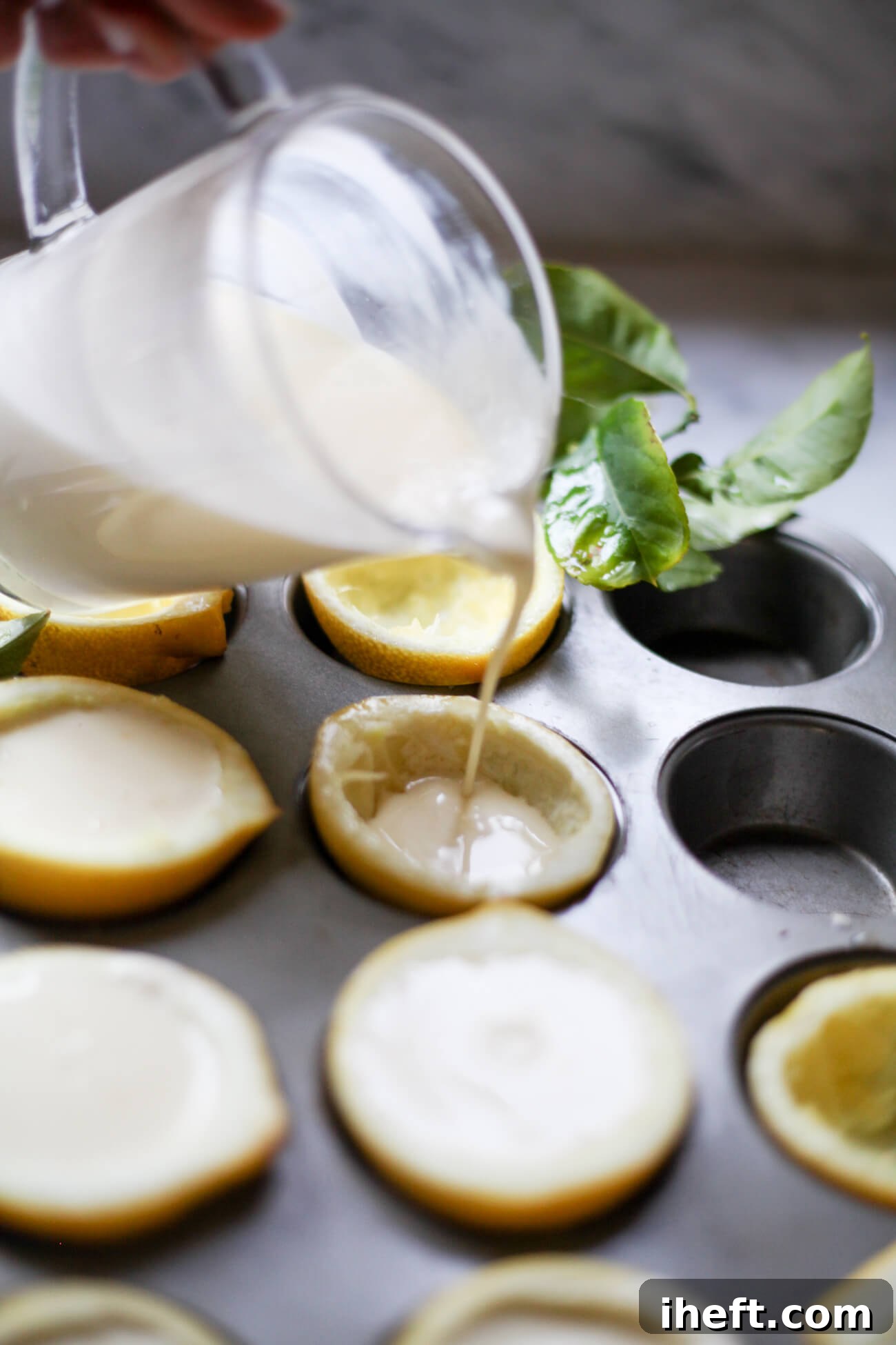 Lemon cream is poured from a glass measuring cup into lemon shells in a muffin pan.
