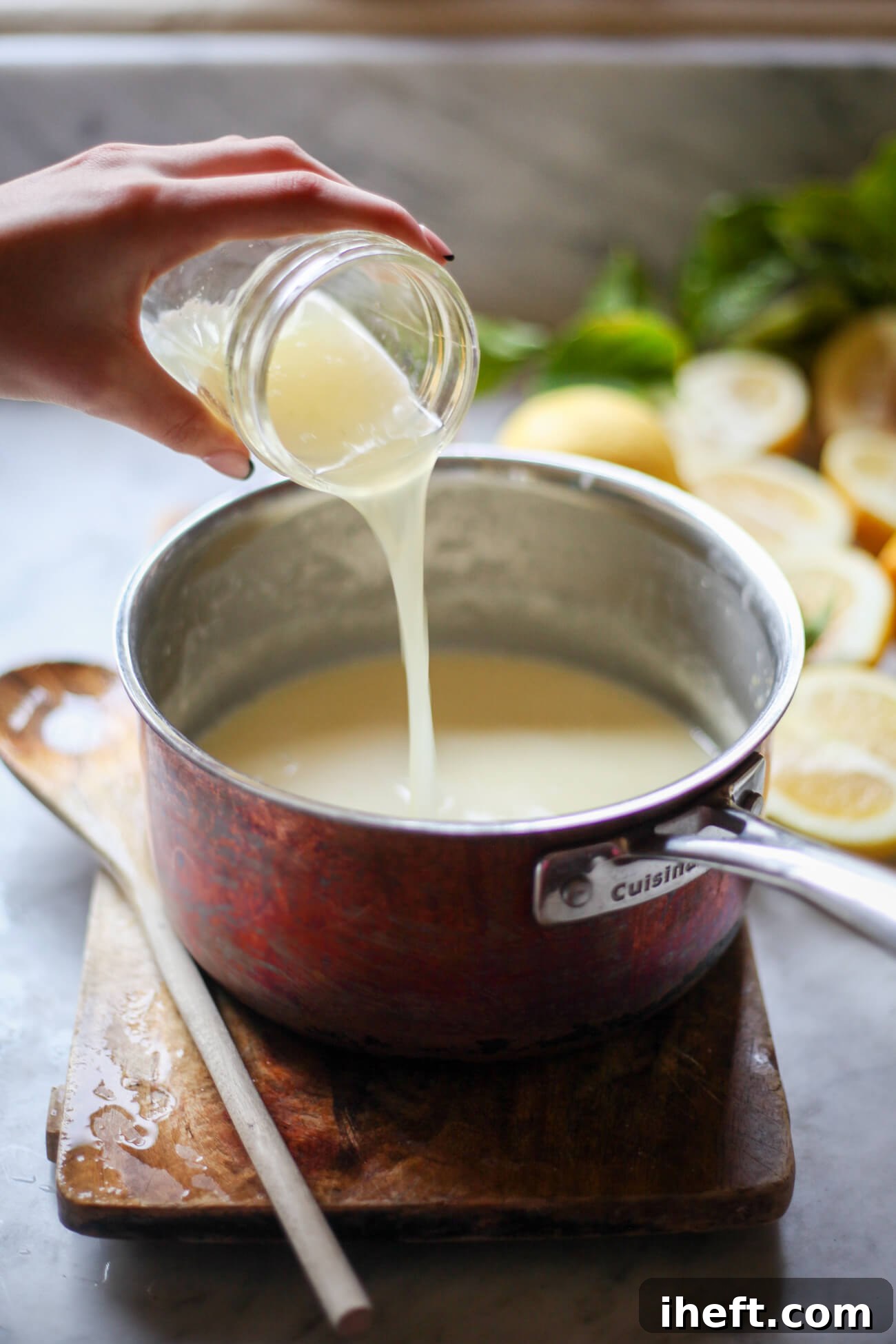 A hand pours fresh lemon juice into a saucepan of hot sugar and cream. 