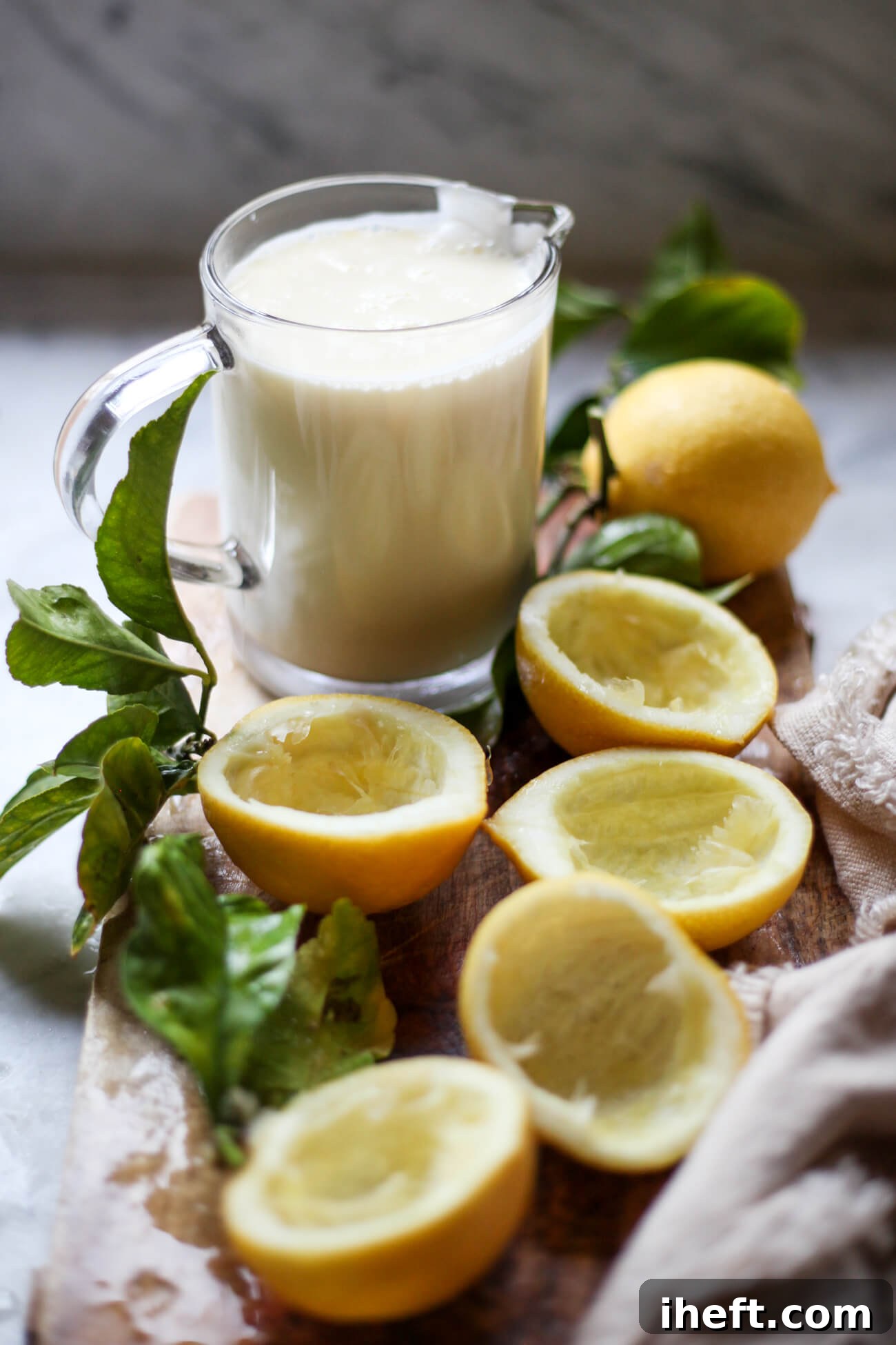 A wooden cutting board filled with hollowed out lemon halves and a glass measuring cup filled with lemon posset cream. 