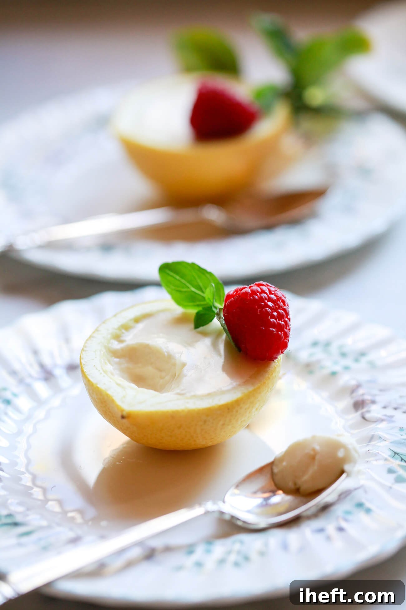A lemon posset in a lemon shell with a scoop taken out with a silver tea spoon. This is a beautiful easy British lemon dessert topped with a raspberry and served on English china dessert plates. 