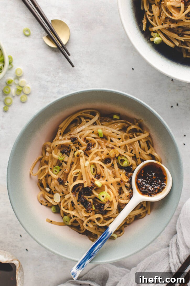 A vibrant bowl of spicy chili garlic noodles, beautifully garnished with fresh green onions and a side of extra chili oil for those who crave more heat. A perfect quick and easy weeknight meal.