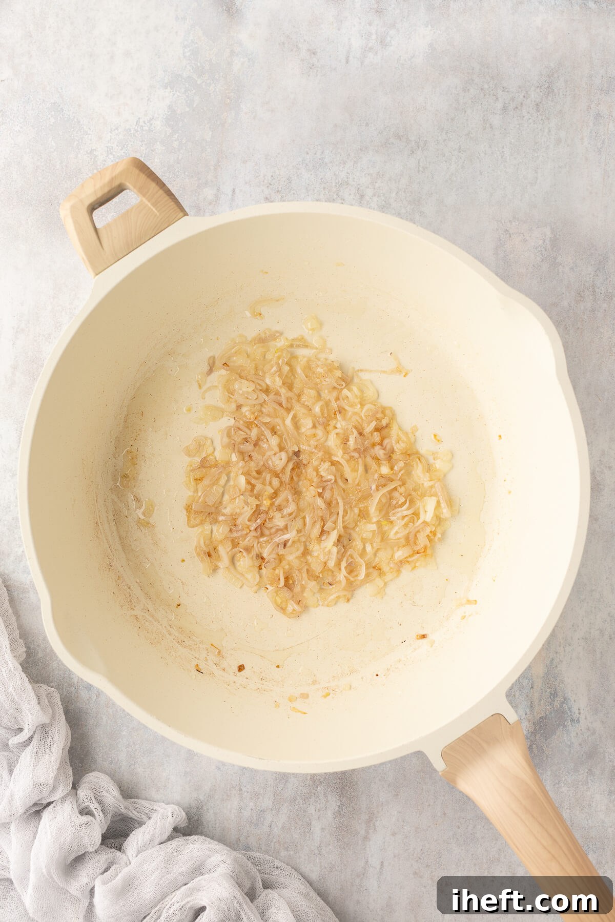 Thinly sliced shallots are gently cooking in a large white ceramic pan with neutral oil over medium heat, becoming tender and fragrant.