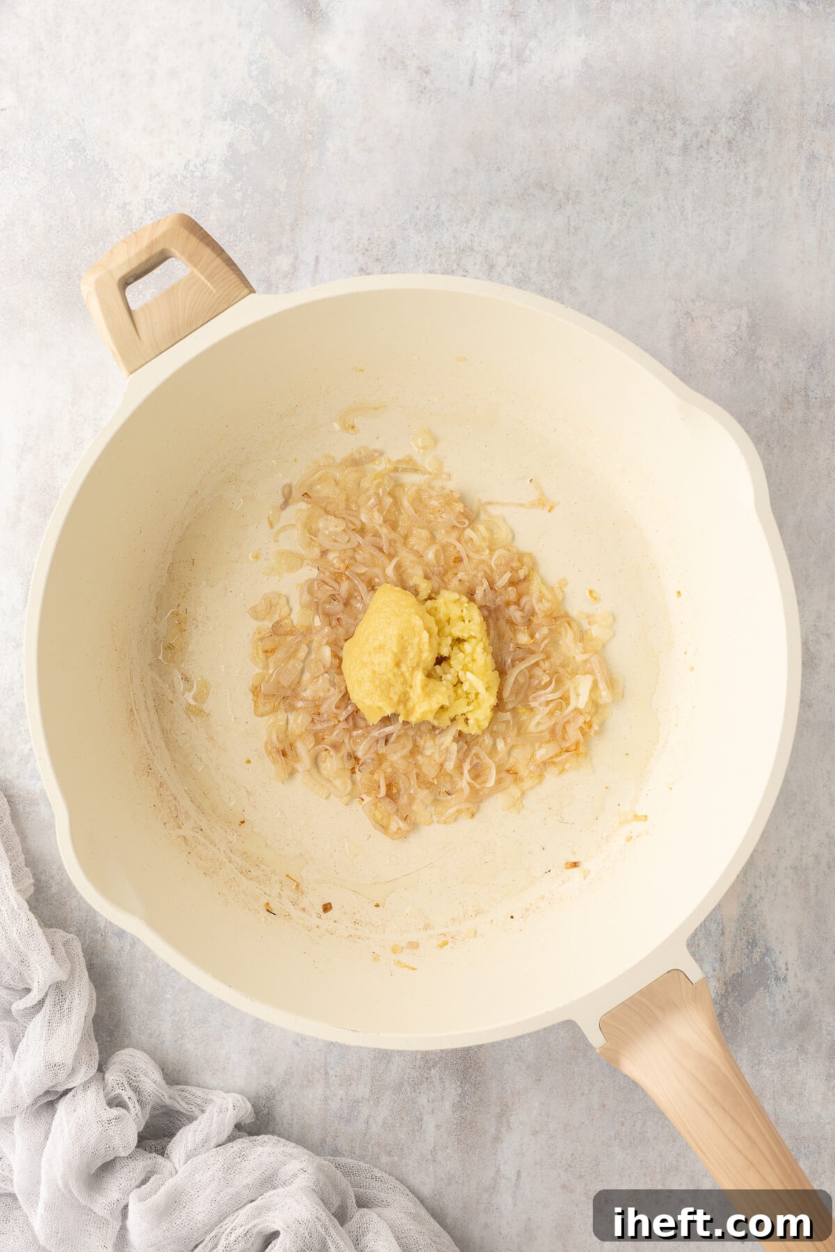 Minced garlic and freshly grated ginger are added to the softened shallots in a ceramic pan, ready to be gently sautéed until fragrant, forming the aromatic base of the dish.