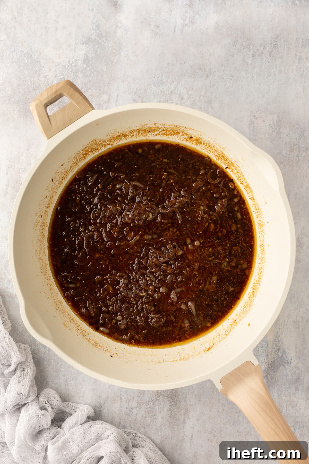 The spicy Asian chili garlic sauce is simmering gently in a large white ceramic pan, allowing its vibrant flavors to meld and creating a beautiful, glossy consistency.