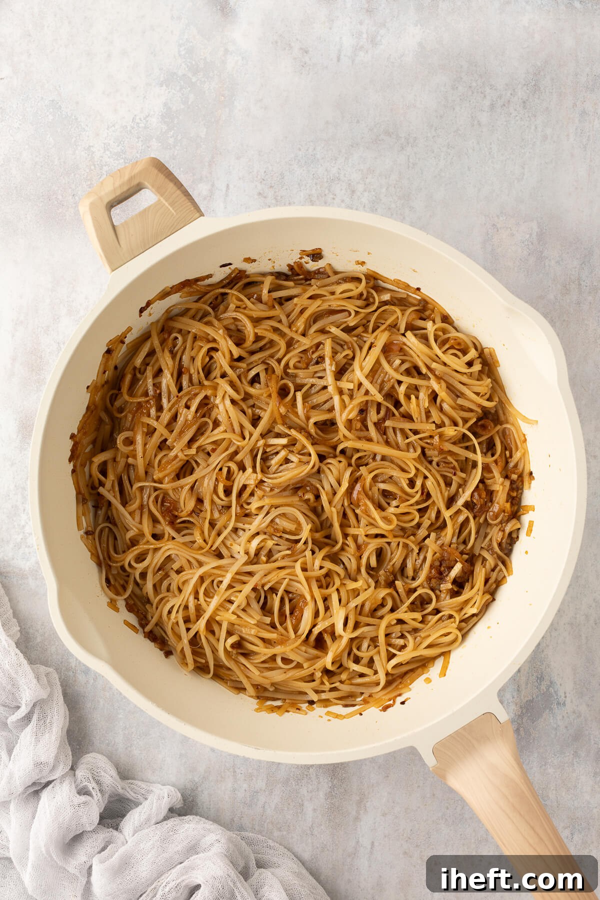 Cooked rice noodles are being vigorously tossed in a ceramic pan, beautifully coated with the vibrant chili garlic sauce, ensuring every strand is infused with flavor.