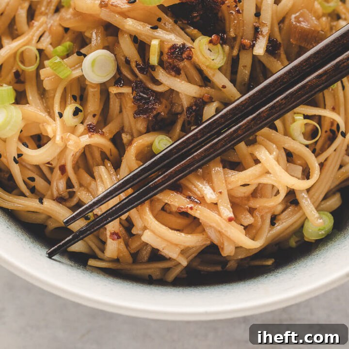 A close-up photo of a bowl of chili garlic noodles with chopsticks, highlighting the glossy sauce and fresh garnishes, ready to be enjoyed.